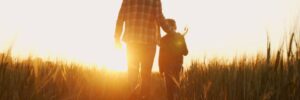 Farmer and his son in front of a sunset agricultural landscape.