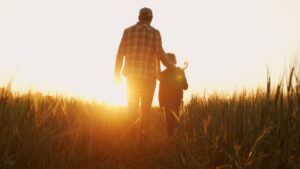 Farmer and his son in front of a sunset agricultural landscape.